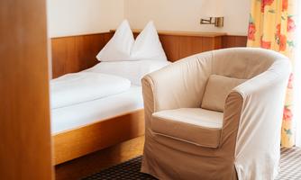 A cozy room with a bed and a comfortable armchair. The windows are decorated with colorful curtains.