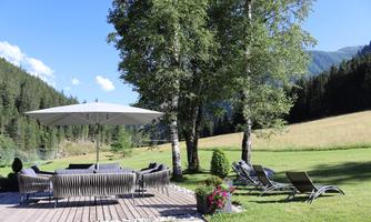 An inviting outdoor area with a large sun umbrella and comfortable lounge furniture. Surrounded by lots of greenery and mountains, ideal for relaxing.