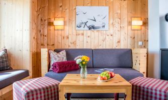 A cozy living room with wooden walls and a comfortable couch. On the table are fruits and a bouquet of flowers.