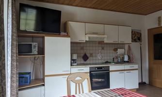 A modern kitchen with bright furniture and appliances. In the foreground stands a table with a striped tablecloth.