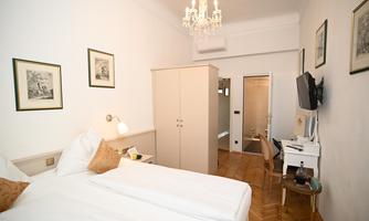 A cozy bedroom with two single beds, a small desk, and a modern TV. The walls are decorated with pictures, and the furniture is kept light.