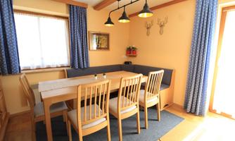 A cozy dining area with a large table and chairs. The walls are painted in warm colors and there are windows with curtains.