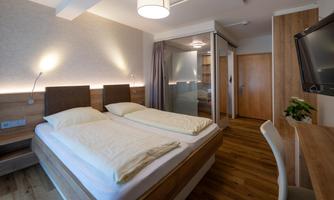 A modern bedroom with two single beds and warm wooden details. The lighting creates a cozy atmosphere.