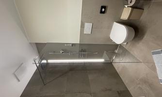 A modern bathroom with a walk-in shower and a toilet. The walls are in neutral gray tones and there is natural lighting.