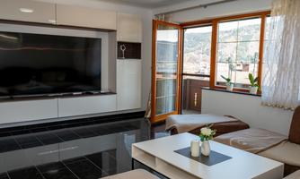 A modern living room with a large television and a bright window front. The room has elegant furniture and a beautiful view outside.
