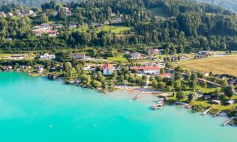 A picturesque landscape with a clear, turquoise lake. Surrounded by green forests and charming houses.