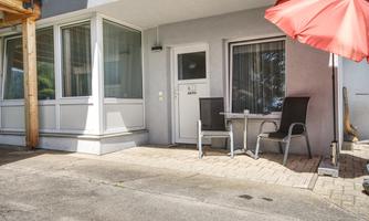 An entrance to an apartment with a small terrace. Two chairs and a table are under a red parasol.