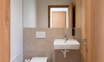 A modern bathroom with a toilet and a sink. The walls are light and the door is made of wood.