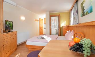 A cozy room with wooden furniture, a bed, and a table. On the table, there is a fruit bowl with grapes and apples.