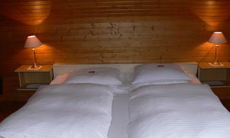 A cozy bedroom with a double bed and white bedcovers. On the sides, there are nightstands with lamps.