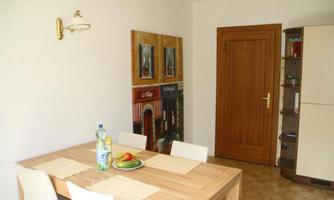 A simple dining area with a wooden table and white chairs. Pictures are hanging on the wall and a door leads to another room.