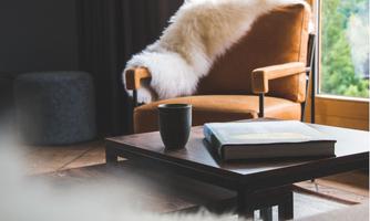 A cozy living space with an orange armchair and a soft sheepskin. On the table, there is a cup and a book.