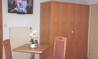 A cozy room with a table and two chairs. A television hangs on the wall, and a dresser stands next to a radiator.