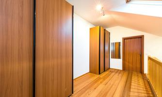A bright room with wooden flooring and large wooden cabinets. The walls are plain and there is a window that lets in natural light.