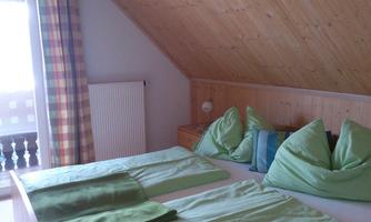 A cozy bedroom in the attic with a double bed and green pillows. Large windows provide plenty of light.