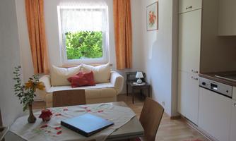 A bright apartment with a cozy sofa and a dining table. The room has large windows with a view of greenery.