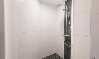 A modern shower with white tiles and a dark wall. The shower is equipped with a comfortable shower head.