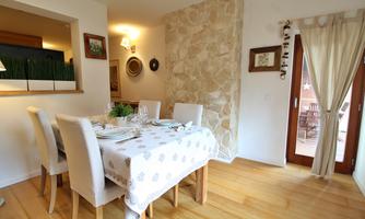A brightly lit dining area with a wooden floor and an elegant table. The walls are decorated with artwork and a stone wall element.