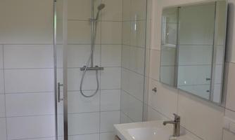 A modern bathroom with a glass door shower and a wooden sink. White tiles and a neutral color tone create a bright ambiance.