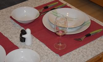 A set table with white plates, cutlery, and a glass of wine. Salt and pepper shakers are also present.