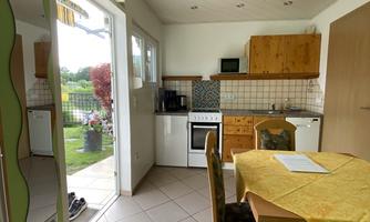 A bright kitchen with wooden cabinets and a dining table. It leads to a small outdoor area overlooking the garden.