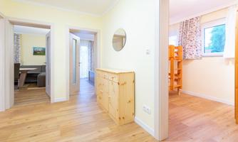 A bright hallway with wooden flooring and yellow walls. On the left is a wooden cabinet and on the right is a child's bed in an adjacent room.
