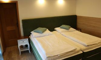 A cozy bedroom with two single beds and bright walls. There is a small nightstand and a wooden floor.