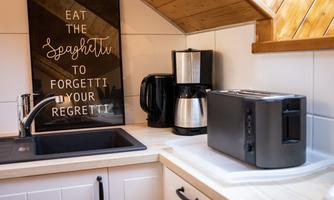 A modern kitchen with a sink, a coffee machine, and a toaster. On the wall hangs a funny sign with the saying "Eat the spaghetti to forget your regret."
