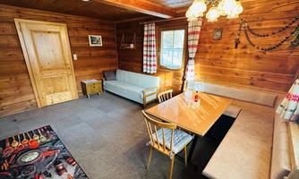 A cozy room with wooden walls and a large table.  
There is a sofa, windows with curtains, and a decorative ceiling lamp.
