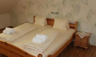A cozy bedroom with a double bed and two pillows. The walls are lightly decorated and next to the bed is a nightstand.
