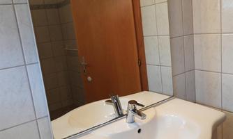 A bathroom with a sink and a mirror. The walls are tiled and a wooden door leads to another room.