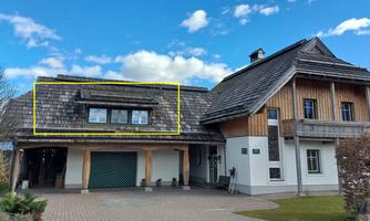 A modern house in a rural style with wooden cladding and a greened entrance. The sky is clear and the architecture is appealing.