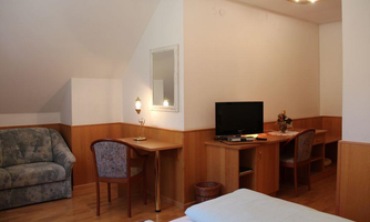 A cozy room with wooden furniture, a TV, and a desk. The room design is bright and inviting.
