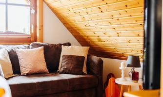 A cozy living room with a brown sofa and decorative cushions. A small table with a lamp and decorative pieces complements the space.