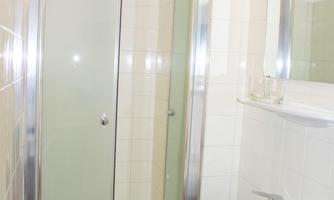 A small bathroom with a shower, a sink, and a mirror. The walls are brightly tiled and well lit.