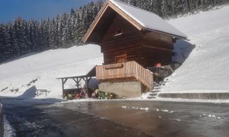 A cozy wooden house on a snowy meadow. In the background, there are tall trees covered with snow.