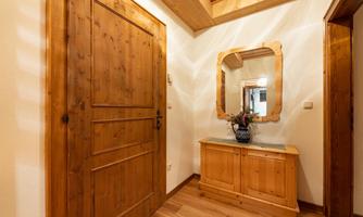 An inviting hallway with a wooden door and a large mirror. On the dresser, there is a flower vase, and the room has a warm, cozy atmosphere.