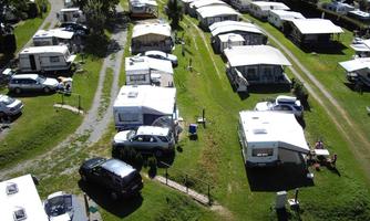 A campsite with several caravans and tents on green grass. Cars are also parked on the premises.