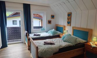A cozy bedroom with two single beds and a modern, bright design. Large windows provide plenty of daylight and a view of the outdoor area.
