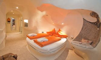 A modern hotel room with organic shapes and warm colors. The room is furnished with a comfortable bed and cozy pillows.