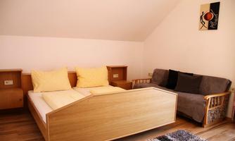 A cozy bedroom with a wooden bed and yellow pillows. There is a sofa and a wooden dresser that make the room feel inviting.