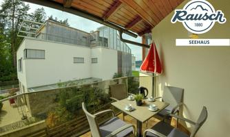 A cozy balcony with a table and chairs, ideal for having breakfast outdoors. In the background, a modern building and green spaces are visible.