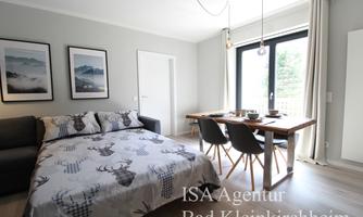 A modern living studio with a cozy bed and a dining table. Large windows let in plenty of light and offer a view of nature.