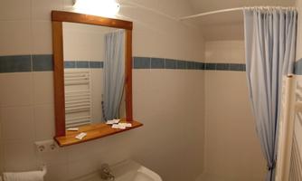 A simple bathroom with a sink, a mirror, and a shower cubicle. The walls are tiled in light colors, and a blue shower curtain hangs.