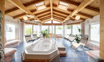 A beautiful wellness area with a hot tub and a wooden ceiling. Hanging chairs and plants create a relaxing atmosphere.