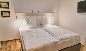 A modern bedroom with a double bed and two pillows. Pictures hang on the walls, and a flat-screen TV is visible.