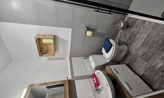 A modern bathroom with a shower, a sink, and a toilet. The walls are bright and the floor has an elegant gray tile covering.