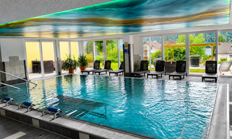 A modern indoor pool with clear water and a stylish deck. Large windows provide a view of the outside and ensure plenty of daylight.