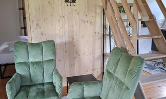 A cozy room with two green armchairs and a wooden wall. In the background, stairs and a gray carpet are visible.