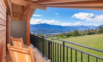 A cozy balcony with two loungers and a view of the mountains and the green valley. The sky is clear and sunny.